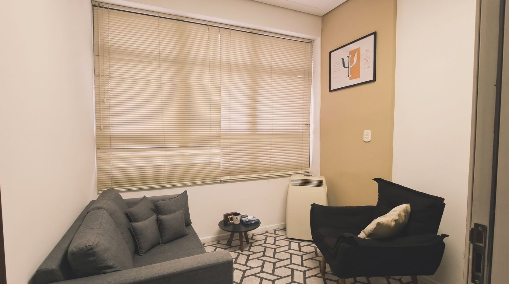 Sala de atendimento do consultório de psicologia, com sofá, poltrona e quadro com o símbolo da psicologia